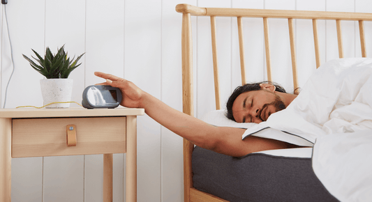 picture of a guy turning off his alarm clock having had a great nights sleep on his hybrid mattress