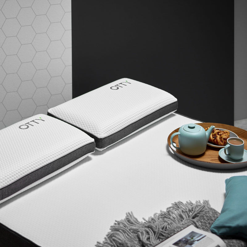 a pair of memory foam pillows on top of our hybrid mattress with a rather nice looking pastry, cup of tea and teapot on a tray laying on the bed as well 