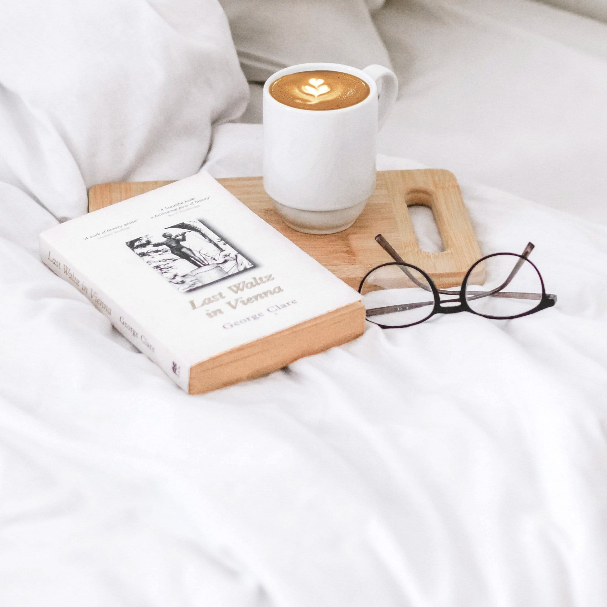 picture of our white beddings duvet cover with a book, reading glasses and a precariously place full cup of coffee on a board which has the potential to ruin the lovely white bedding cotton.